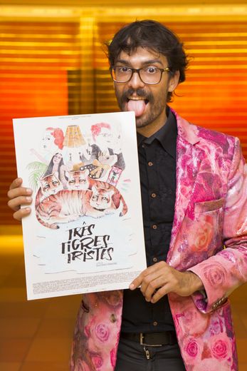 A man in a colourful suit jacket is holding up a poster, laughing and nibbling on the corner of the poster.