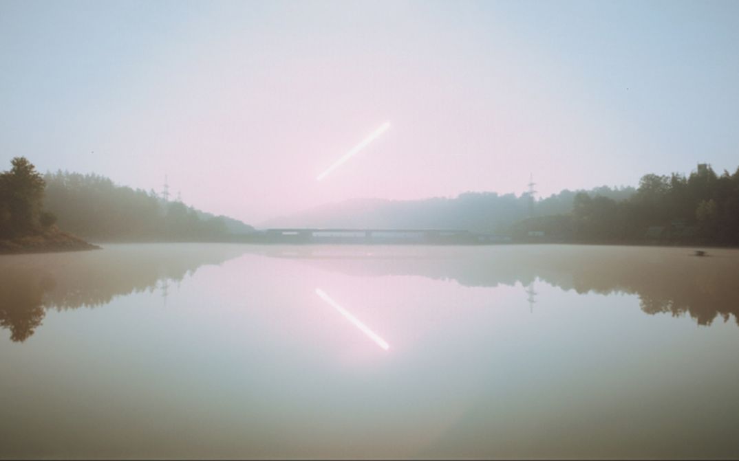 Film Still aus dem Film „Forever…Forever“ von Johann Lurf. Eine weitläufige, ruhige Landschaft mit Wasser und Himmel, die nahezu ineinander übergehen. Die Szene wirkt hell, weich und entrückt. Über der horizontalen Linie von Ufern und Brücke zieht ein schräger Lichtstrahl durch den Himmel und spiegelt sich im Wasser darunter.