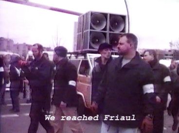 Still from the film "Normality 1–X" by Hito Steyerl. People at a demonstration with the speaker van and organizers. 