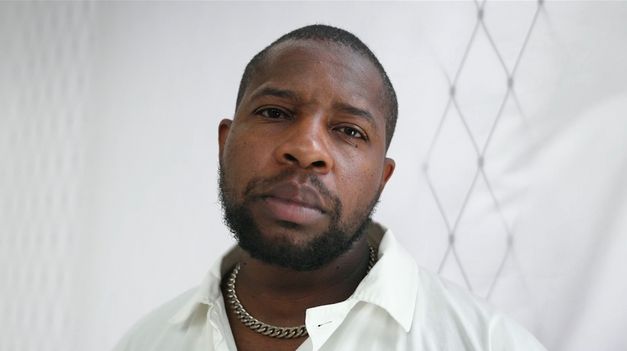 Still from the Film "Jail Bird in a Peacock Chair" by James Gregory Atkinson. A man looks directly into the camera.