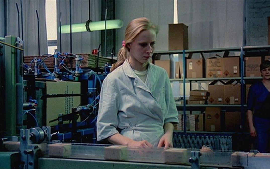 Filmstill aus DAS MÄDCHEN AUS DER STREICHHOLZFABRIK: Eine junge Frau steht an einem Fließband in einer Fabrik.