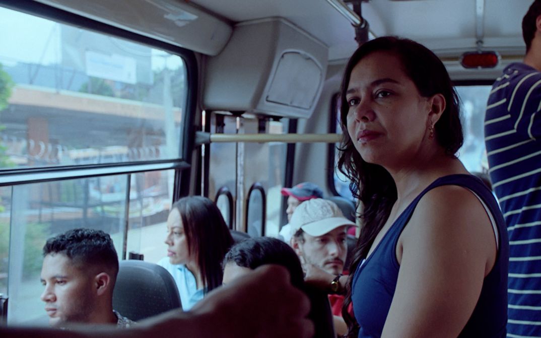 Filmstill aus "La piel en primavera" von Yennifer Uribe Alzate. Zu sehen ist eine Nahaufnahme einer stehenden Frau in einem Bus. Der Bus ist mit Menschen gefüllt.