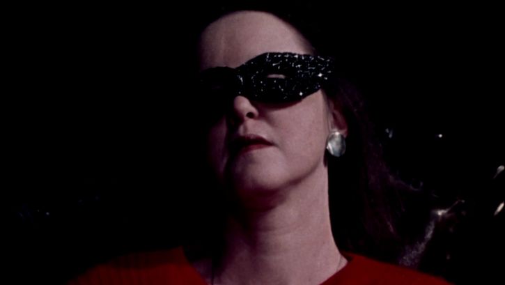 Film still from CHANGE OF FATE: You see the face of a woman with a black mask around her eyes.