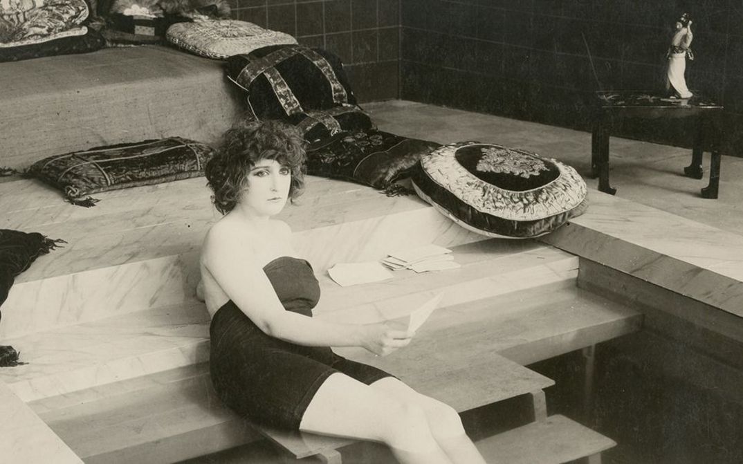 Film still aus LA BELLE DAME SANS MERCI: A young woman sits on the stairs in a glamorous house.