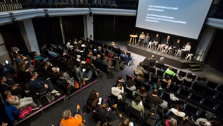Ein Podiumsdiskussion im silent green Kulturquartier, fotografiert von oben herab auf den gefüllten Veranstaltungssaal, auf einer Bühne sitzen sechs Personen.