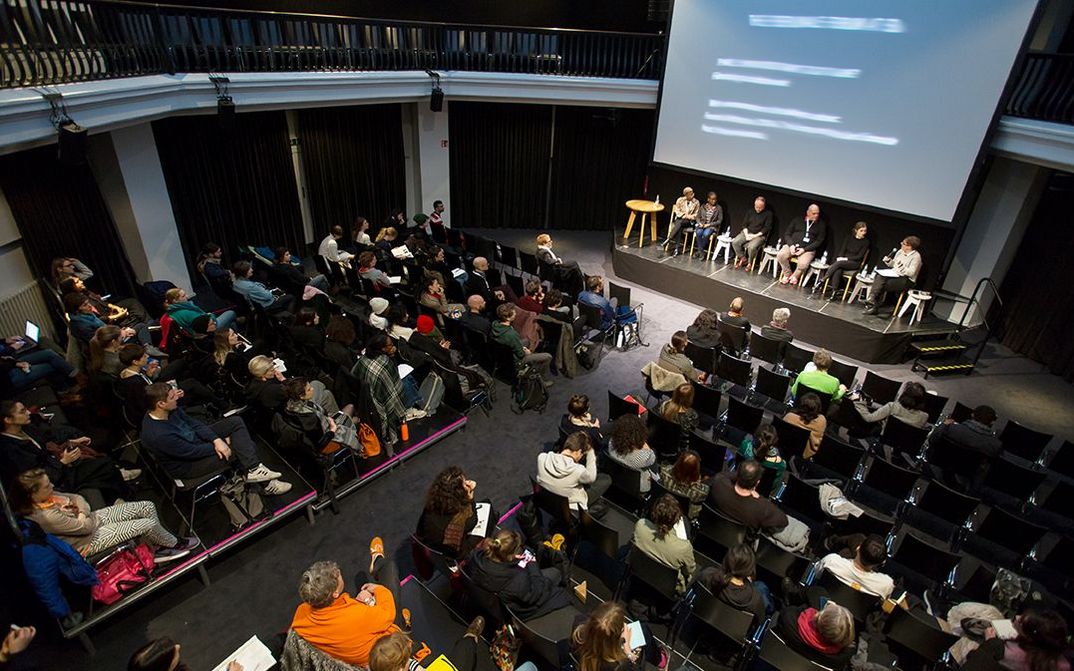 Ein Podiumsdiskussion im silent green Kulturquartier, fotografiert von oben herab auf den gefüllten Veranstaltungssaal, auf einer Bühne sitzen sechs Personen.
