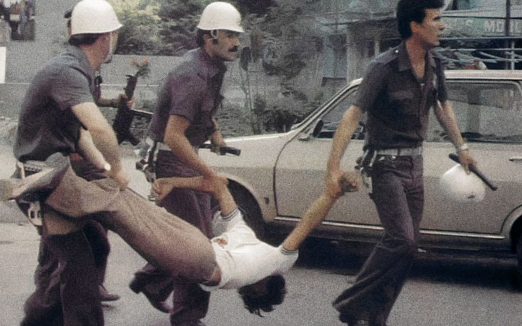 Three uniformed men (policemen) carry a man by his arms and legs.