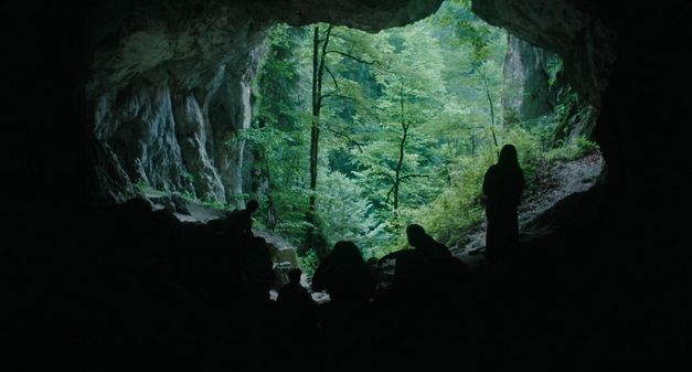 Mehrere Personen stehen als Silhouetten in einer Höhle und blicken nach draußen.