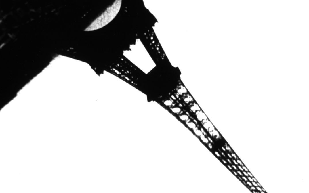 Film still from JEUX DES REFLETS ET DE VITESSE: A black-and-white photograph of the Eiffel Tower, which extends diagonally from the top left to the bottom right of the image.