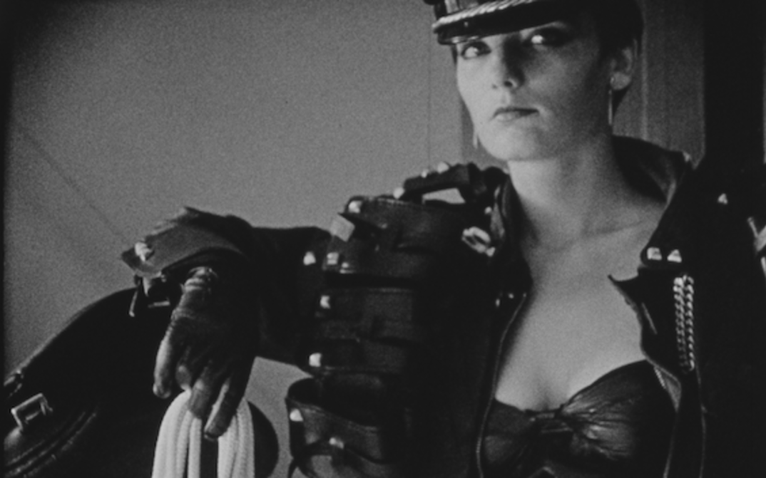Filmstill aus MANO DESTRA: Eine Frau in Leder gekleidet und mit einem Seil in der Hand blickt in die Kamera.
