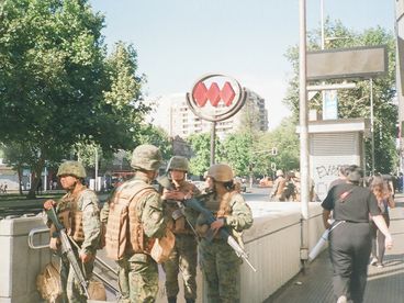 35-mm-Farbfoto. Vier junge Soldaten stehen an einem sonnigen Tag vor dem Eingang einer U-Bahn-Station. Im Hintergrund sind Zivilpersonen und weitere Soldaten zu sehen.