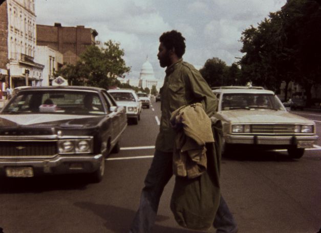 Filmstill aus ASHES AND EMBERS: Ein Mann überquert eine Straße, im Hintergrund ist das Kapitol in Washington zu sehen.