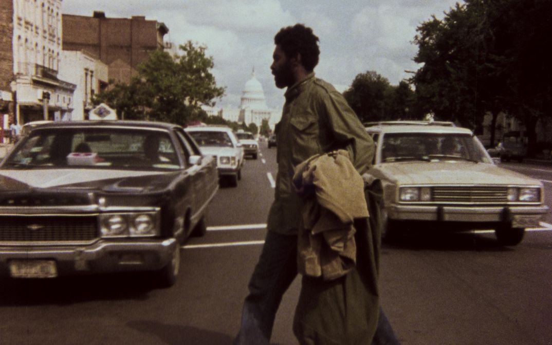 Film still from ASHES AND EMBERS: A man crosses a street, the Capitol in Washington can be seen in the background.