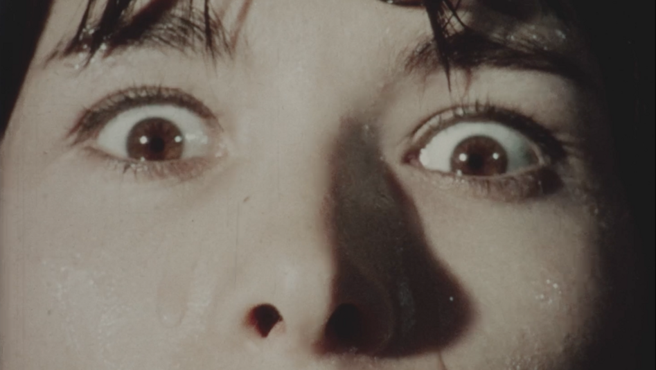 Film still from PHOBIE D'IMPULSION: A close-up of a woman's face. Her eyes are wide with fear, and tears are streaming down her cheeks.