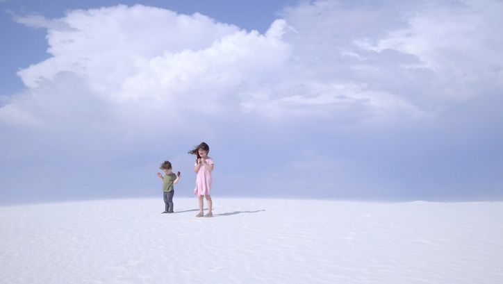 Filmstill aus „Nuclear Family“ von Erin Wilkerson und Travis Wilkerson. Zwei Kinder stehen auf einer Sanddüne vor blauem Himmel.