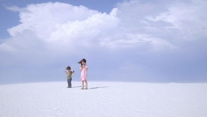 Filmstill aus „Nuclear Family“ von Erin Wilkerson und Travis Wilkerson. Zwei Kinder stehen auf einer Sanddüne vor blauem Himmel.