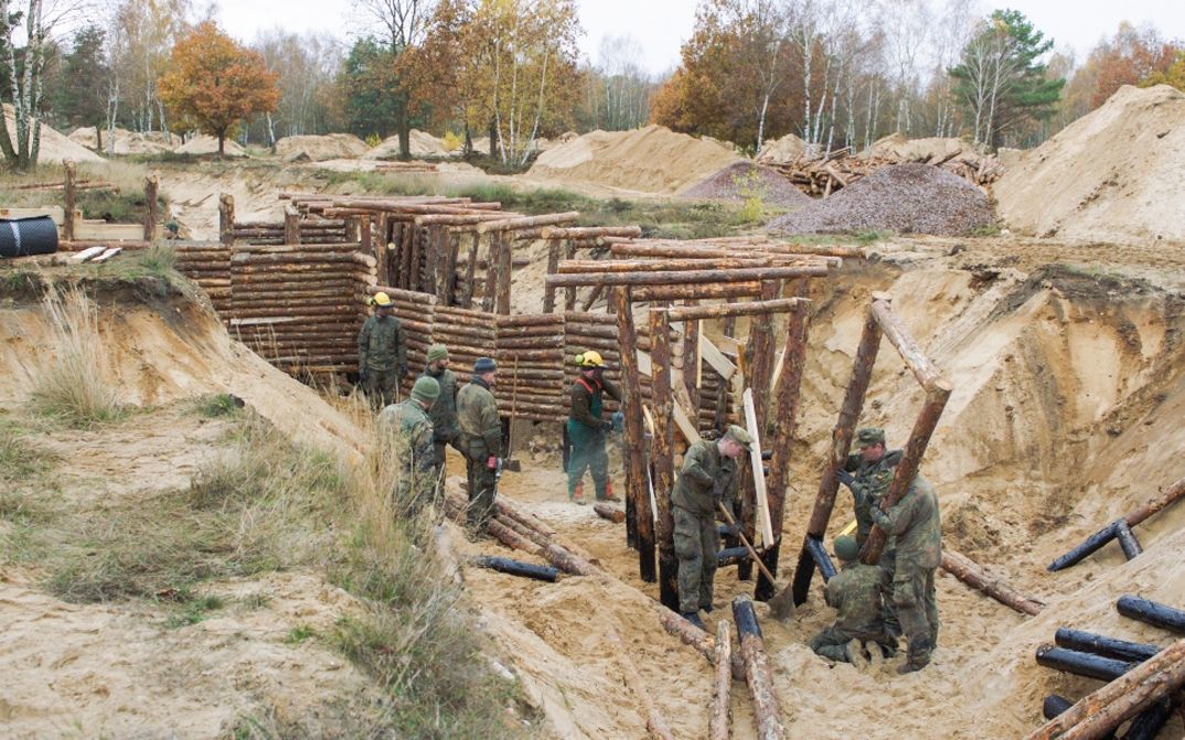 Soldaten bauen Holzbefestigungen in sandigem Gelände mit Werkzeugen.