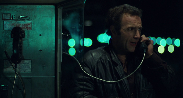 Still from "Thief" by Michael Mann. A man is standing by a public pay phone, speaking and looking off to the side. The light is moody. it is night, in the background we see blue city lights.