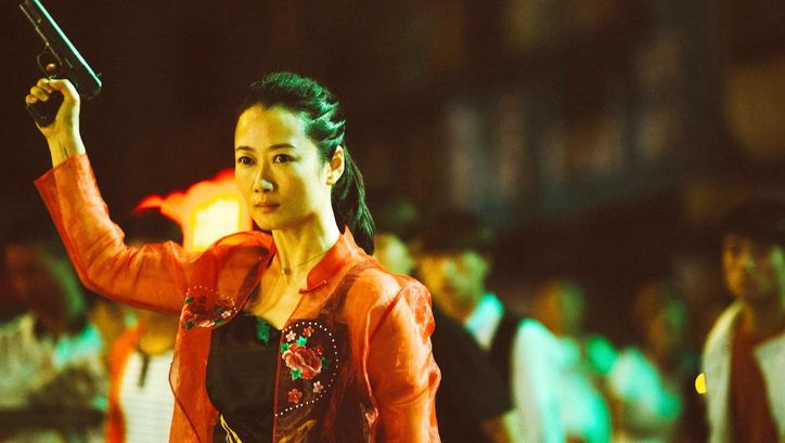 Filmstill aus ASH IS PUREST WHITE: Eine Frau in roter Bluse mit ernstem Blick hebt eine Pistole in die Luft.