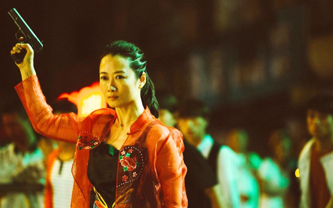 Filmstill from ASH IS PUREST WHITE: A woman in a red blouse with a serious look on her face raises a pistol in the air.