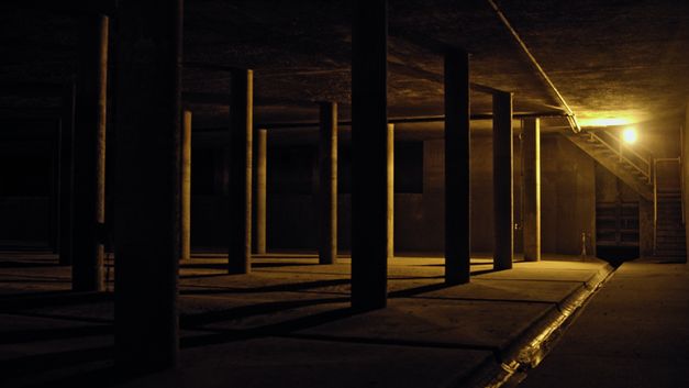 Still from the film "Voices and Shells" by Maya Schweizer. A dark, covered hall with columns.