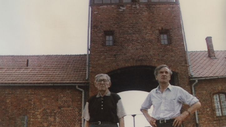 Filmstill aus TO SPEAK THE UNSPEAKABLE – THE MESSAGE OF ELIE WIESEL: Elie Wiesel und ein Begleiter stehen als Besucher im KZ Auschwitz.