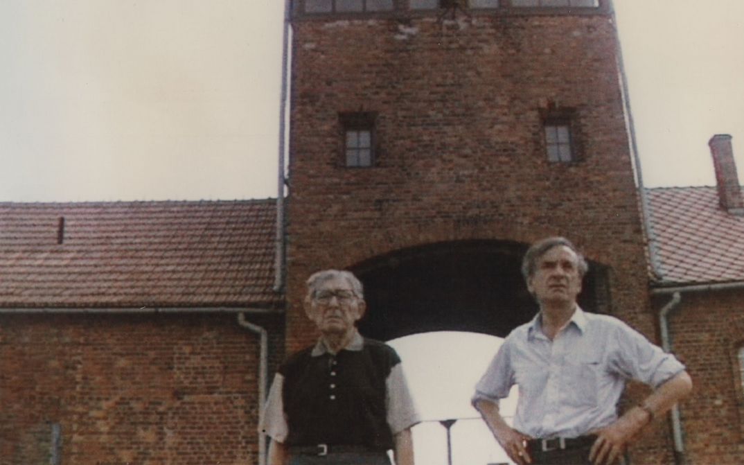 Filmstill aus TO SPEAK THE UNSPEAKABLE – THE MESSAGE OF ELIE WIESEL: Elie Wiesel und ein Begleiter stehen als Besucher im KZ Auschwitz.