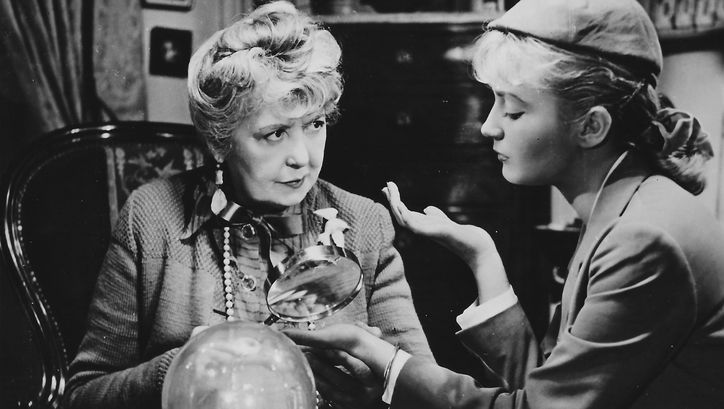 Film still from SOUS LE CIEL DE PARIS COULE LA SEINE: An older and a younger woman sit together at a table.