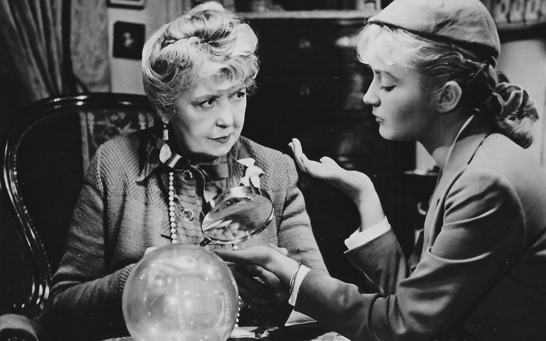 Film still from SOUS LE CIEL DE PARIS COULE LA SEINE: An older and a younger woman sit together at a table.