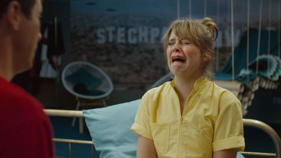 Film still from ZWEI IM FALSCHEN FILM: Laura Tonke, wearing a yellow top, is crying in a theatrical manner.