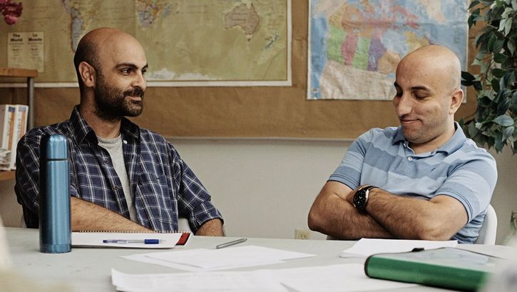 Filmstill from „Concrete Valley" by Antoine Bourges. Two men are sitting at a table in a classroom and are talking happily.