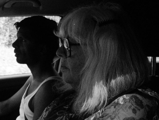 Eine Frau und ein Mann sitzen nebeneinander im Auto, im Profil gesehen, Licht fällt durch die Seitenscheibe.