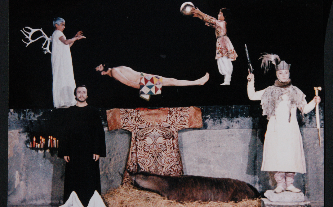 Filmstill aus SAJAT NOVA: Ein surrealistisches Tableau mit mehreren Figuren vor einem dunklen Hintergrund.