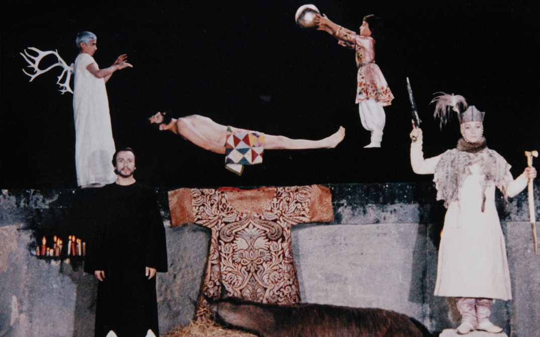 Filmstill aus SAJAT NOVA: Ein surrealistisches Tableau mit mehreren Figuren vor einem dunklen Hintergrund.