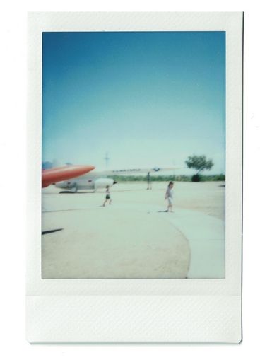 Polaroid of two children running around a display of missiles and airplanes. 