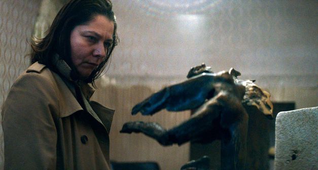 Eine Frau in einem Innenraum betrachtet eine schwebende menschliche Bronze- oder Messingskulptur mit ausgestreckten Gliedmaßen.