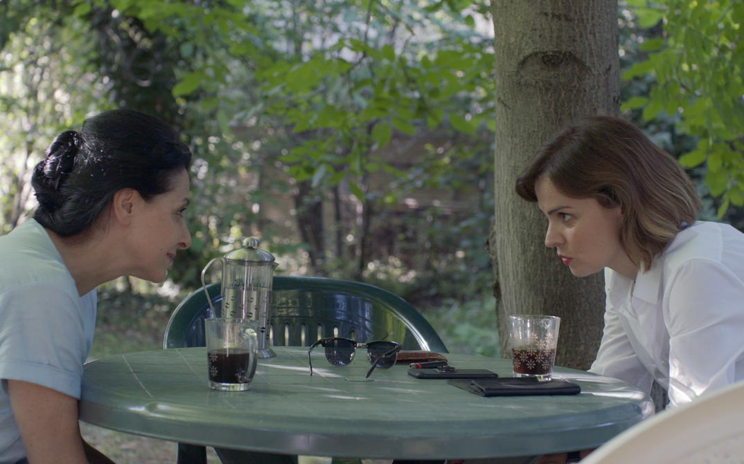Filmstill aus COMETS. Zwei Frauen blicken sich über einen Tisch hinweg an.