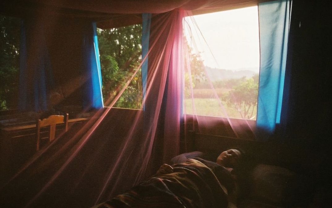 Film still from UNCLE BOONMEE WHO CAN RECALL HIS PAST LIVES: A woman is lying in bed right by the window. Transparent curtains in different colors are hung.