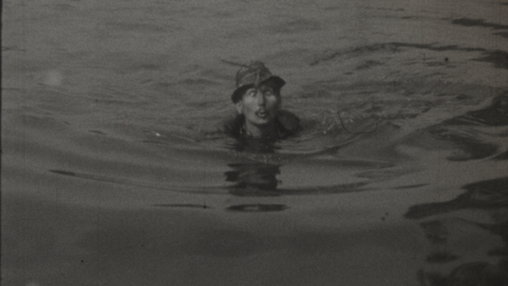 Filmstill aus HASTRMAN: Ein Mann mit Hut schwimmt in in einem Gewässer.