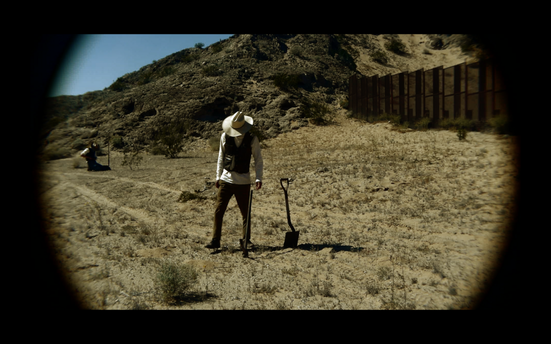 Film still from TERRESTIAL SEA: A person stands in a field and looks down at the ground.