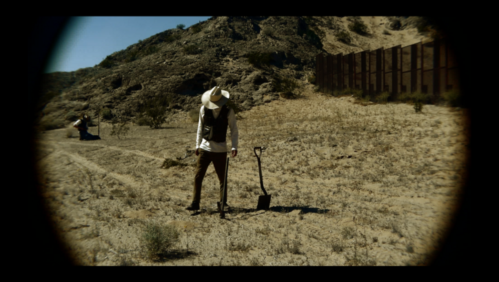 Filmstill aus TERRESTIAL SEA: Eine Person steht auf einem Feld und blickt zu Boden.