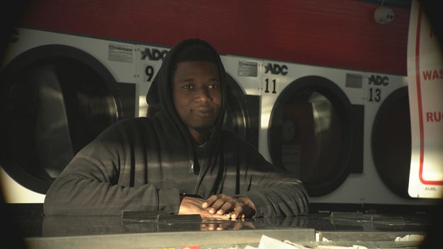 Ein Mann sitzt in Waschsalon vor laufenden Maschinen mit ruhigem Blick.