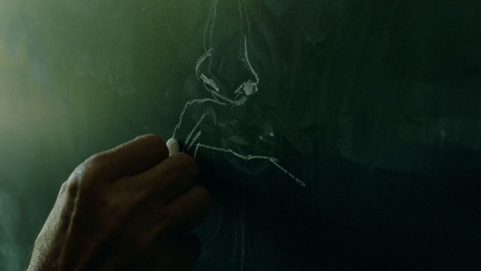 Filmstill aus I believe the portrait saved me: Eine Hand zeichnet mit einer Kreide auf eine Tafel.