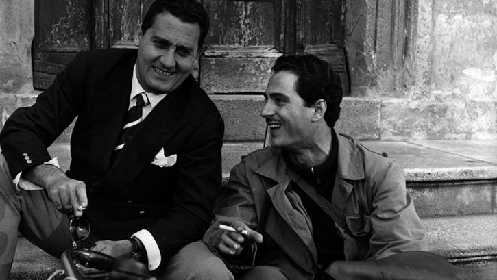 Film still from LO SCAPOLO: Two men are sitting on a staircase laughing and smoking.