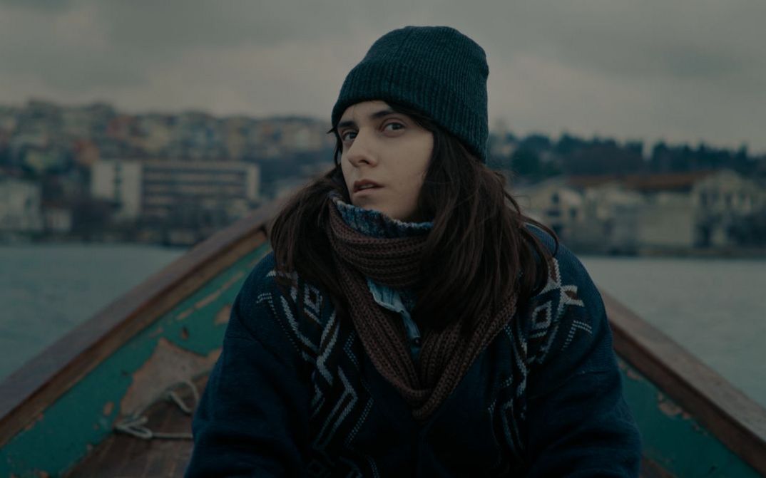 A young woman in winter clothes sits in a small boat and looks sceptically into the camera.