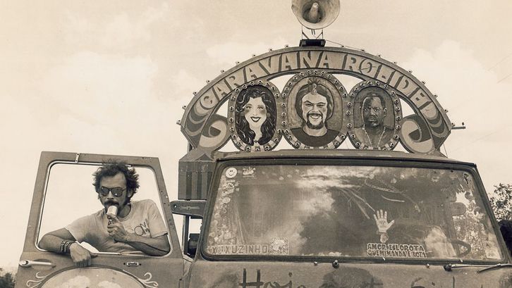 Film still from BYE BYE BRASIL: A man stands in the doorway of a painted car equipped with a loudspeaker.