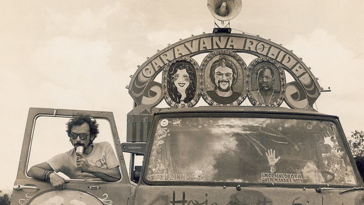 Film still from BYE BYE BRASIL: A man stands in the doorway of a painted car equipped with a loudspeaker.