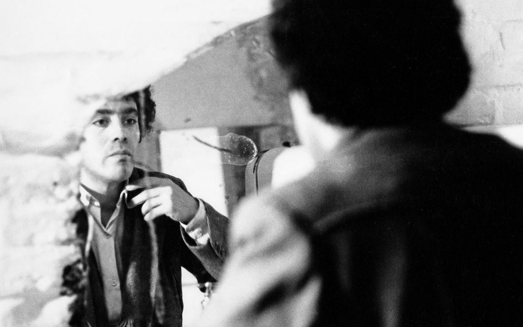 Foto von den Dreharbeiten zu „In der Wüste“ von Rafael Fuster Pardo. Ein Mann schaut sich im Spiegel an und richtet seine Kleidung.