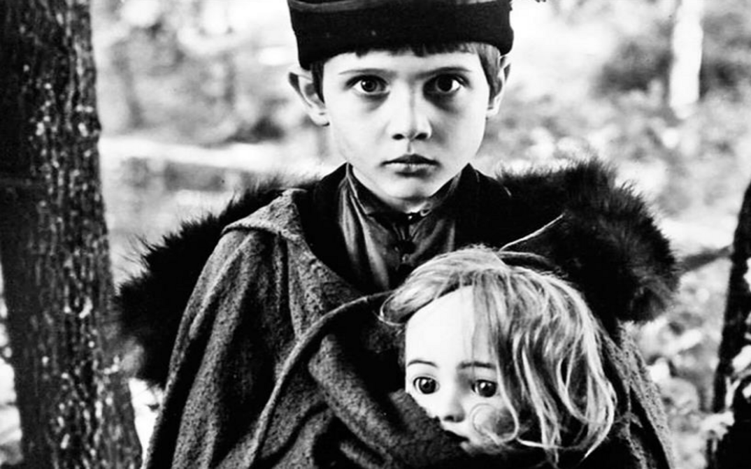 Film still from AMONG GREY STONES: A boy holds a doll in his arms and looks into the camera.