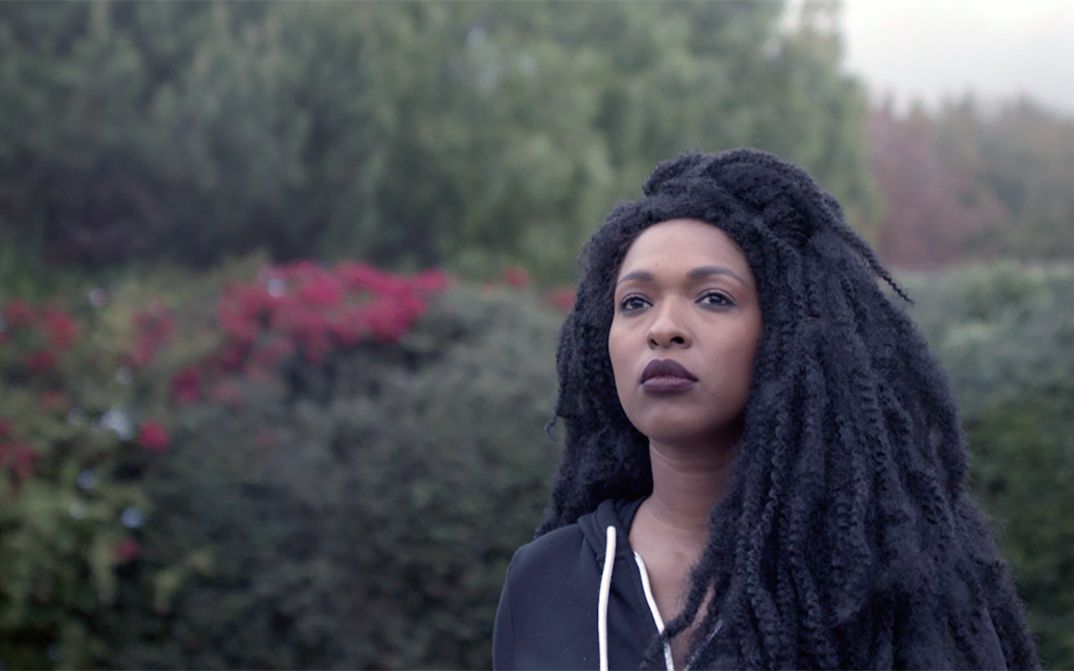 Film still from THE TUBA THIEVES: A young woman stands in the greenery and gazes into the distance.